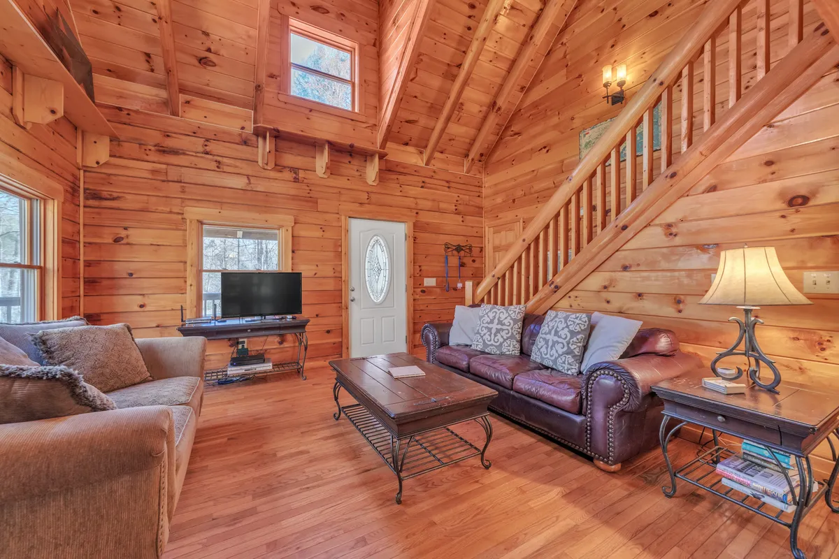 A cozy living space featuring a sofa, coffee table, TV, and wooden staircase. The room exudes warmth and is set up for relaxing, socializing, and casual group activities such as family game nights.