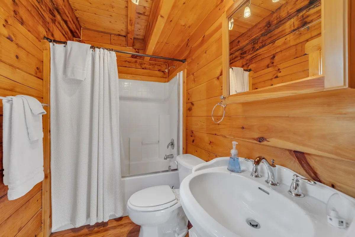 A bright bathroom featuring rustic wooden walls, a large mirror, a sink, and a modern shower area. The inviting fixtures and soft lighting create a spa-like feel, perfect for relaxation after outdoor adventures.