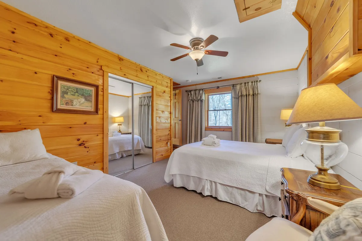 A comfortable bedroom with two beds, warm wood paneling, a window draped with curtains, a bedside lamp, and a mirror. The space feels restful and ideal for families or groups, reflecting the flexibility mentioned in the section.