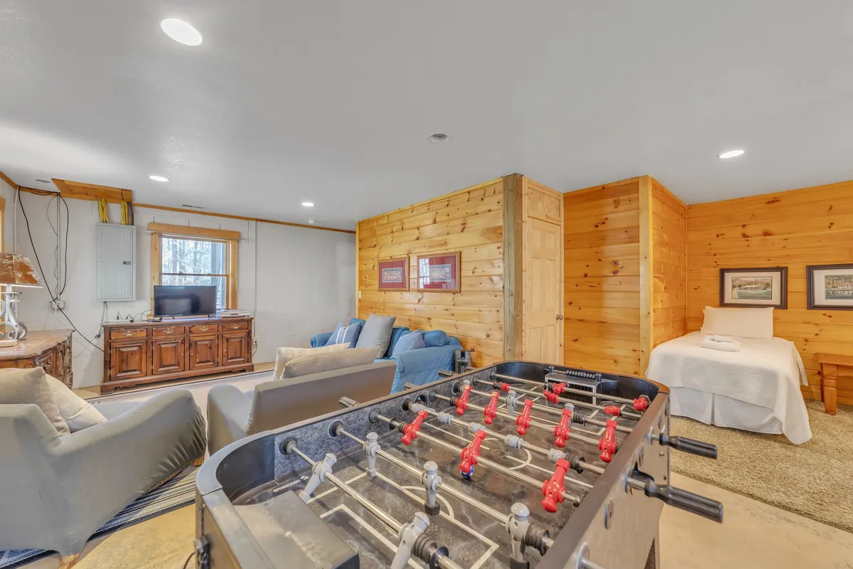 A lively basement playroom scene with a foosball table as the focal point, blue couches for lounging, wood paneled walls, and a television for entertainment. The setup feels casual and inviting, ideal for playful competitions and group activities.